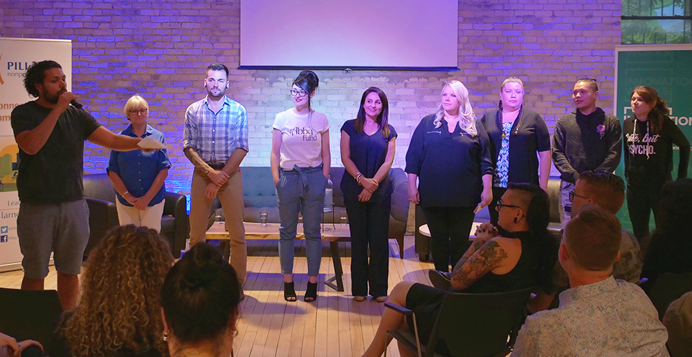 Emcee at an event speaking to audience, alongside 8 social entrepreneurs on stage